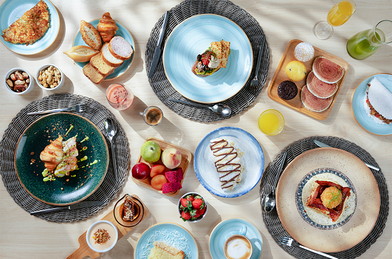 Uma grande mesa de café da manhã all inclusive com gastronomia diversa: pães, croissants, frutas frescas, tapioca, ovos, sucos e café.
