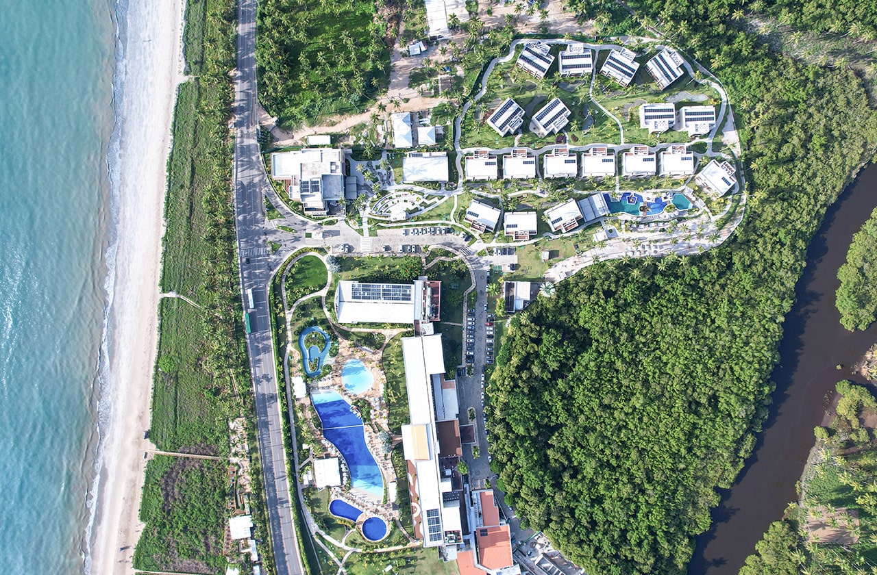 Japaratinga Lounge Resort com vista de cima, mostrando o complexo entre a praia com água bem azul e o rio, cercado por uma natureza paradisíaca bem verde.
